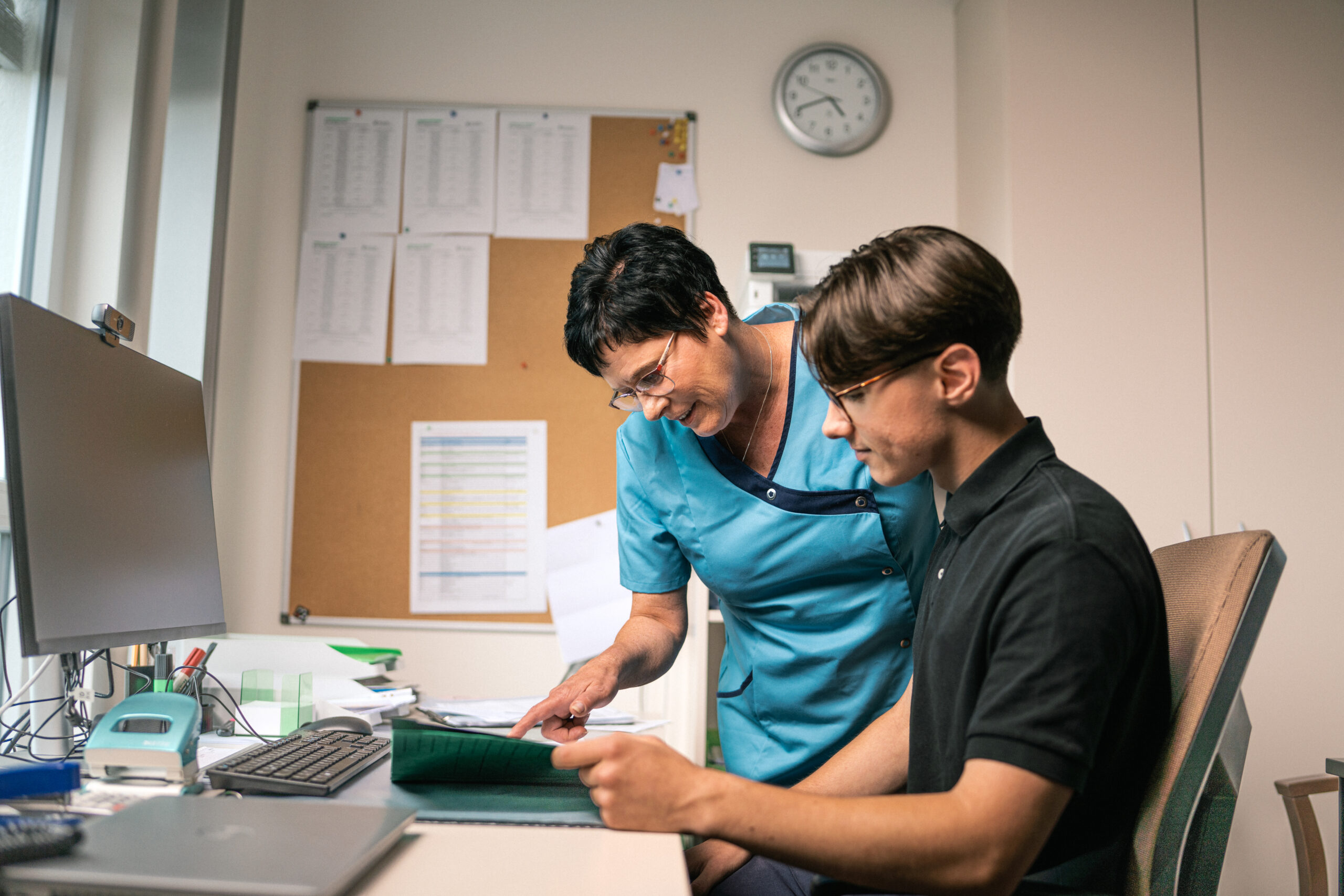 Eine Frau erklärt dem Auszubildenen etwas am Schreibtisch im Büro