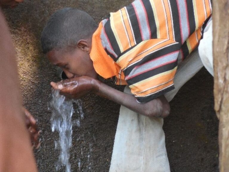 äthipisches Kind trinkt Wasser direkt aus einem Wasserhahn der Teil eines umgesetzten Brunnenprojekts ist.