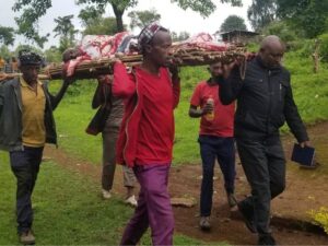 Ein Patient wird von vier Männern auf einer einfachen Trage aus Ästen in die Krankenstation getragen