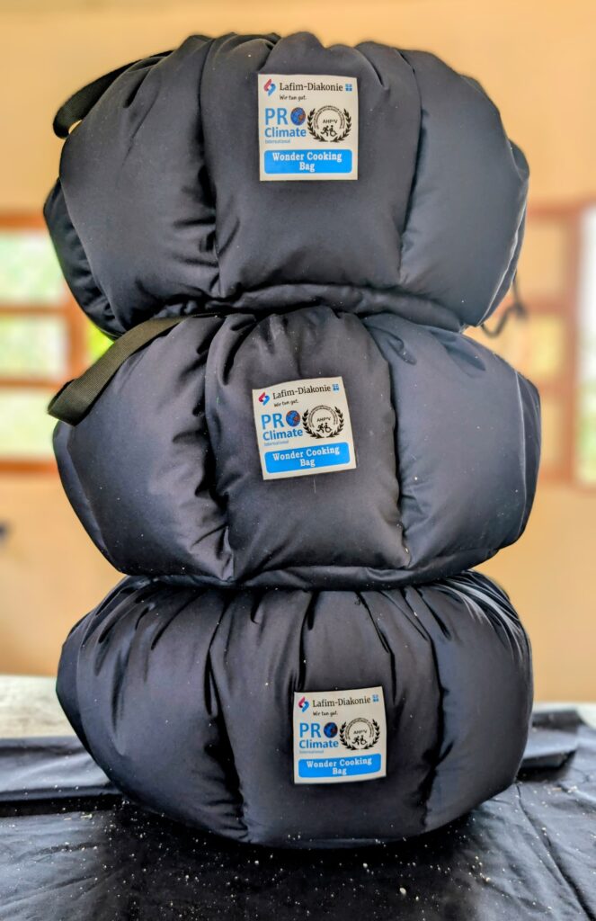 Drei gestalpelte Klimakocher genäht aus schwarzem, feuerfestem Stoff und Aufnäher mit den Logos von PCI, AHPPV und Lafim-Diakonie