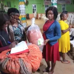 Workshop mit Frauengruppe bei welchem der Klima-Kocher präsentiert wurde. Man sieht eine Frau mit Klima-Kocher auf dem Arm in einer Halle mit vielen Menschen